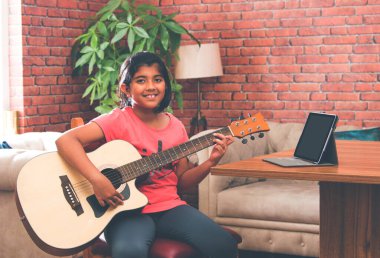 Asyalı Hintli çocuk evde bilgisayar ya da tablet kullanarak müzik ya da müzik aleti öğreniyor, hobiyi ikna ediyor