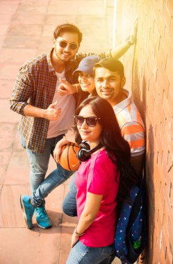 Kolej öğrencilerinden oluşan neşeli Hintli genç bir grup ya da arkadaşlar kampüste otururken, ayakta ya da yürürken birlikte gülüyorlar.