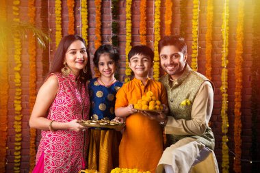 Diwali veya Rakshabandhan Kutlaması - Dört kişilik Hint ailesi Deepavali veya Bhai Dooj festivalini tatlı laddoo, yağ lambası ve şeker ve şeker kutuları ile kutluyor, yemek yiyor veya selfie çekiyor