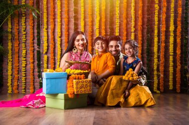 Diwali veya Rakshabandhan Kutlaması - Dört kişilik Hint ailesi Deepavali veya Bhai Dooj festivalini tatlı laddoo, yağ lambası ve şeker ve şeker kutuları ile kutluyor, yemek yiyor veya selfie çekiyor
