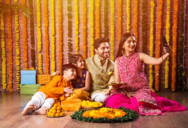 Diwali veya Rakshabandhan Kutlaması - Dört kişilik Hint ailesi Deepavali veya Bhai Dooj festivalini tatlı laddoo, yağ lambası ve şeker ve şeker kutuları ile kutluyor, yemek yiyor veya selfie çekiyor