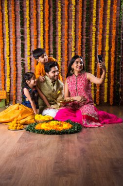 Diwali veya Rakshabandhan Kutlaması - Dört kişilik Hint ailesi Deepavali veya Bhai Dooj festivalini tatlı laddoo, yağ lambası ve şeker ve şeker kutuları ile kutluyor, yemek yiyor veya selfie çekiyor