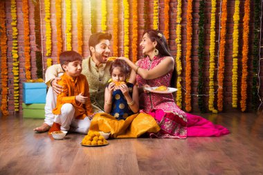 Diwali veya Rakshabandhan Kutlaması - Dört kişilik Hint ailesi Deepavali veya Bhai Dooj festivalini tatlı laddoo, yağ lambası ve şeker ve şeker kutuları ile kutluyor, yemek yiyor veya selfie çekiyor
