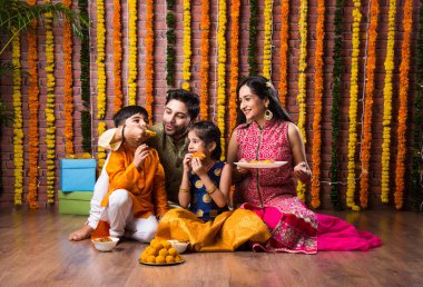 Diwali veya Rakshabandhan Kutlaması - Dört kişilik Hint ailesi Deepavali veya Bhai Dooj festivalini tatlı laddoo, yağ lambası ve şeker ve şeker kutuları ile kutluyor, yemek yiyor veya selfie çekiyor