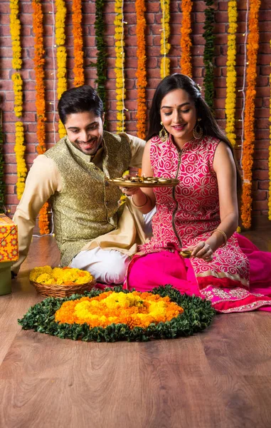 伝統的な服のインドの魅力的なカップルは マリゴールドの花で装飾された背景に驚きの贈り物と甘いラドゥとディワリ祭 誕生日や記念日を祝います — ストック写真
