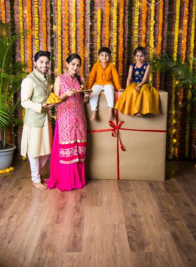 Diwali veya Rakshabandhan Kutlaması - Dört kişilik Hint ailesi Deepavali veya Bhai Dooj festivalini tatlı laddoo, yağ lambası ve şeker ve şeker kutuları ile kutluyor, yemek yiyor veya selfie çekiyor