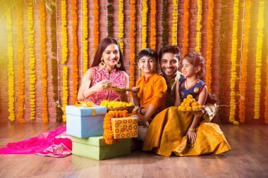 Diwali veya Rakshabandhan Kutlaması - Dört kişilik Hint ailesi Deepavali veya Bhai Dooj festivalini tatlı laddoo, yağ lambası ve şeker ve şeker kutuları ile kutluyor, yemek yiyor veya selfie çekiyor