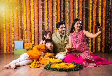 Diwali veya Rakshabandhan Kutlaması - Dört kişilik Hint ailesi Deepavali veya Bhai Dooj festivalini tatlı laddoo, yağ lambası ve şeker ve şeker kutuları ile kutluyor, yemek yiyor veya selfie çekiyor