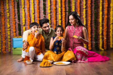 Diwali veya Rakshabandhan Kutlaması - Dört kişilik Hint ailesi Deepavali veya Bhai Dooj festivalini tatlı laddoo, yağ lambası ve şeker ve şeker kutuları ile kutluyor, yemek yiyor veya selfie çekiyor
