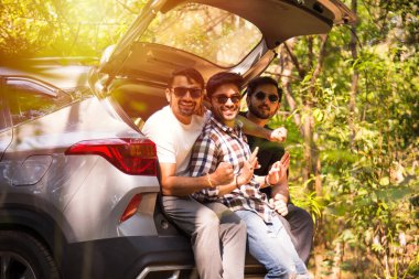 Bir grup Hintli Asyalı genç ve çekici arkadaş bir arabanın bagajında oturuyorlar, yaz gezisi.