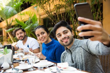 Bir grup genç Hintli Asyalı öğle yemeği ya da kahvaltı yapıyor, adam selfie çekiyor.  
