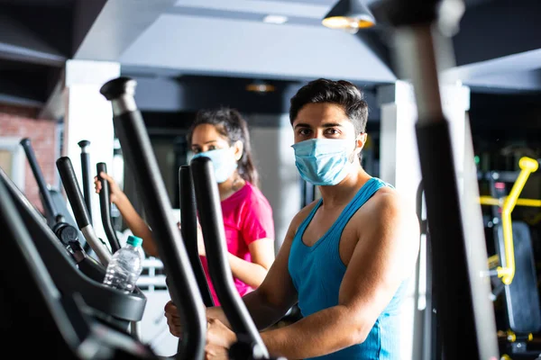 gym after corona - Indian young couple working out in gym post corona outbreak, wears protective face mask