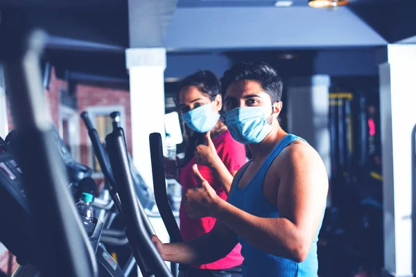 gym after corona - Indian young couple working out in gym post corona outbreak, wears protective face mask