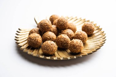 Sesame seed jaggery ball or til ke laddo and tilgul or til gul laddu served in bowl for Makar Sankranti Festival in India clipart