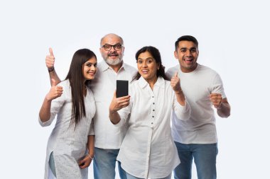Hintli genç bir çift, anne ve babası mutlu ifadelerle akıllı telefon kullanıyor ya da ellerinde tutuyorlar, beyazların karşısında duruyorlar.