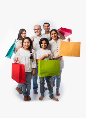 Beyaz arka planda tek başına dururken ellerinde kağıt alışveriş torbaları ve bankamatik ya da kredi kartı tutan çok nesilli mutlu Hintli aile.