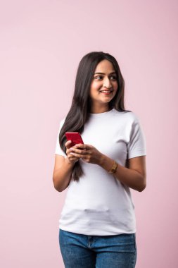 Pembe stüdyoda izole edilmiş bir Hintli kız cep telefonundan mesaj atıyor ya da kablosuz bağlantı ile akıllı telefon kullanıyor.