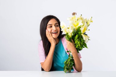 Masada ya da masada beyaz arka planda tek başına otururken elinde çiçek buketi tutan çekici bir Hintli kadının portresini yakından çek.