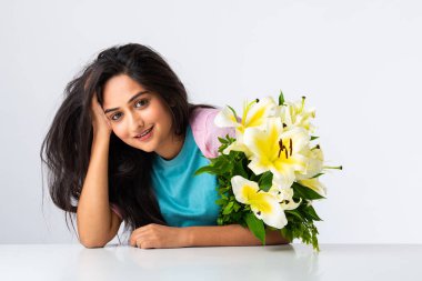 Masada ya da masada beyaz arka planda tek başına otururken elinde çiçek buketi tutan çekici bir Hintli kadının portresini yakından çek.