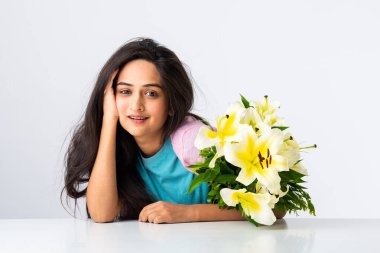 Masada ya da masada beyaz arka planda tek başına otururken elinde çiçek buketi tutan çekici bir Hintli kadının portresini yakından çek.