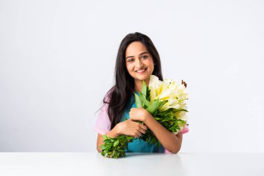 Masada ya da masada beyaz arka planda tek başına otururken elinde çiçek buketi tutan çekici bir Hintli kadının portresini yakından çek.