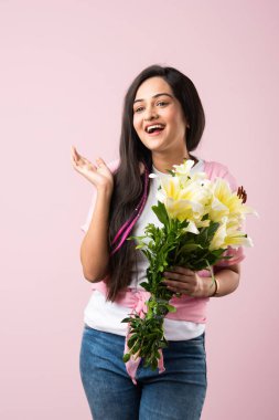 Çekici bir Hintli kadının portresi. Elinde çiçek buketi var. Pembe arka planda tek başına duruyor.