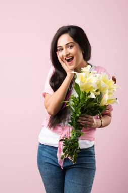 Çekici bir Hintli kadının portresi. Elinde çiçek buketi var. Pembe arka planda tek başına duruyor.