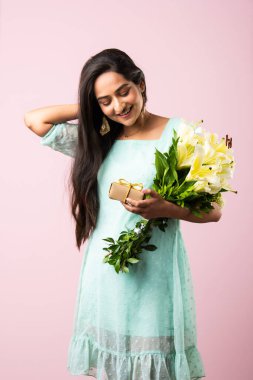 Çekici genç bir Hintli kadının portresi. Elinde çiçek buketi tutarken hediye kutusunu açıyor. Pembe arka planda tek başına duruyor.