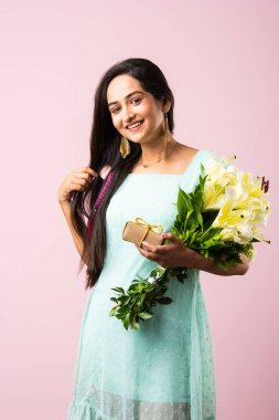 Çekici genç bir Hintli kadının portresi. Elinde çiçek buketi tutarken hediye kutusunu açıyor. Pembe arka planda tek başına duruyor.