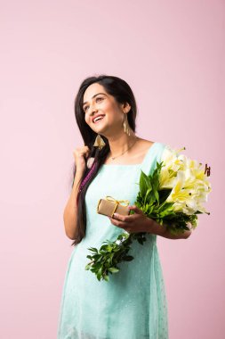 Çekici genç bir Hintli kadının portresi. Elinde çiçek buketi tutarken hediye kutusunu açıyor. Pembe arka planda tek başına duruyor.