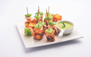 Aperatif aperatif Paneer Tikka beyaz arka planda izole edilmiş yeşil turşulu bir tabakta. Hint mutfağı ızgara süzme peynirli sebze ve baharatlı.