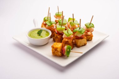 Aperatif aperatif Paneer Tikka beyaz arka planda izole edilmiş yeşil turşulu bir tabakta. Hint mutfağı ızgara süzme peynirli sebze ve baharatlı.