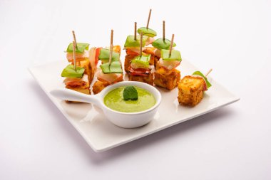 Aperatif aperatif Paneer Tikka beyaz arka planda izole edilmiş yeşil turşulu bir tabakta. Hint mutfağı ızgara süzme peynirli sebze ve baharatlı.