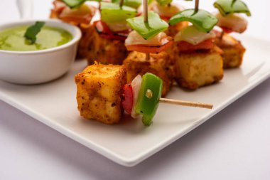 Aperatif aperatif Paneer Tikka beyaz arka planda izole edilmiş yeşil turşulu bir tabakta. Hint mutfağı ızgara süzme peynirli sebze ve baharatlı.