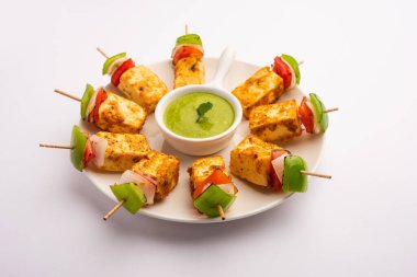 Aperatif aperatif Paneer Tikka beyaz arka planda izole edilmiş yeşil turşulu bir tabakta. Hint mutfağı ızgara süzme peynirli sebze ve baharatlı.