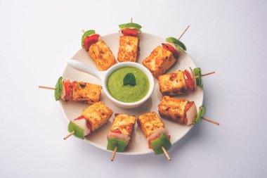 Aperatif aperatif Paneer Tikka beyaz arka planda izole edilmiş yeşil turşulu bir tabakta. Hint mutfağı ızgara süzme peynirli sebze ve baharatlı.