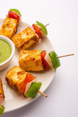 Aperatif aperatif Paneer Tikka beyaz arka planda izole edilmiş yeşil turşulu bir tabakta. Hint mutfağı ızgara süzme peynirli sebze ve baharatlı.