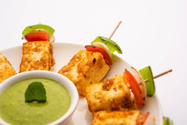 Aperatif aperatif Paneer Tikka beyaz arka planda izole edilmiş yeşil turşulu bir tabakta. Hint mutfağı ızgara süzme peynirli sebze ve baharatlı.