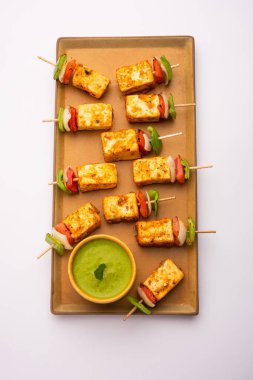 Aperatif aperatif Paneer Tikka beyaz arka planda izole edilmiş yeşil turşulu bir tabakta. Hint mutfağı ızgara süzme peynirli sebze ve baharatlı.