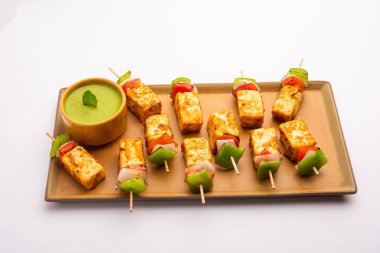 Aperatif aperatif Paneer Tikka beyaz arka planda izole edilmiş yeşil turşulu bir tabakta. Hint mutfağı ızgara süzme peynirli sebze ve baharatlı.