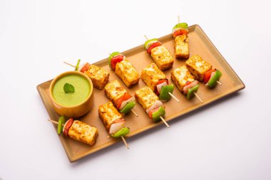 Aperatif aperatif Paneer Tikka beyaz arka planda izole edilmiş yeşil turşulu bir tabakta. Hint mutfağı ızgara süzme peynirli sebze ve baharatlı.