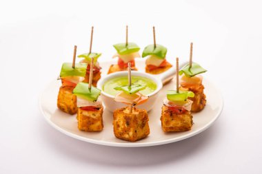 Aperatif aperatif Paneer Tikka beyaz arka planda izole edilmiş yeşil turşulu bir tabakta. Hint mutfağı ızgara süzme peynirli sebze ve baharatlı.