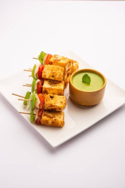 Aperatif aperatif Paneer Tikka beyaz arka planda izole edilmiş yeşil turşulu bir tabakta. Hint mutfağı ızgara süzme peynirli sebze ve baharatlı.