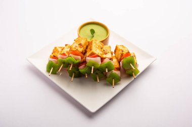 Aperatif aperatif Paneer Tikka beyaz arka planda izole edilmiş yeşil turşulu bir tabakta. Hint mutfağı ızgara süzme peynirli sebze ve baharatlı.
