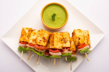Aperatif aperatif Paneer Tikka beyaz arka planda izole edilmiş yeşil turşulu bir tabakta. Hint mutfağı ızgara süzme peynirli sebze ve baharatlı.