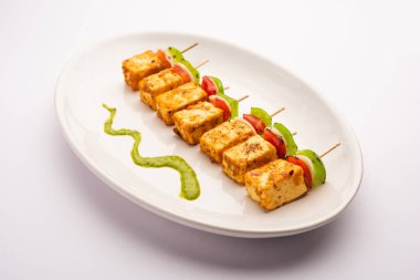 Aperatif aperatif Paneer Tikka beyaz arka planda izole edilmiş yeşil turşulu bir tabakta. Hint mutfağı ızgara süzme peynirli sebze ve baharatlı.