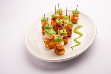 Aperatif aperatif Paneer Tikka beyaz arka planda izole edilmiş yeşil turşulu bir tabakta. Hint mutfağı ızgara süzme peynirli sebze ve baharatlı.