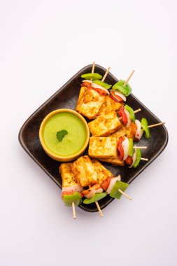 Aperatif aperatif Paneer Tikka beyaz arka planda izole edilmiş yeşil turşulu bir tabakta. Hint mutfağı ızgara süzme peynirli sebze ve baharatlı.