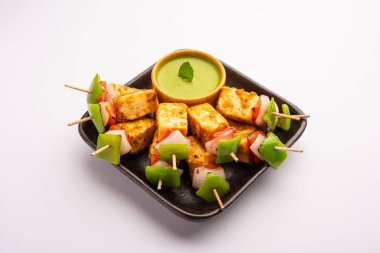 Aperatif aperatif Paneer Tikka beyaz arka planda izole edilmiş yeşil turşulu bir tabakta. Hint mutfağı ızgara süzme peynirli sebze ve baharatlı.