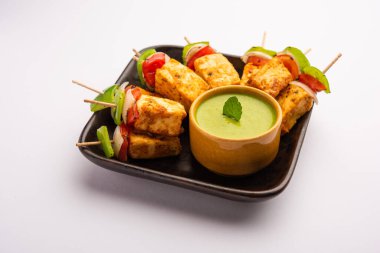 Aperatif aperatif Paneer Tikka beyaz arka planda izole edilmiş yeşil turşulu bir tabakta. Hint mutfağı ızgara süzme peynirli sebze ve baharatlı.